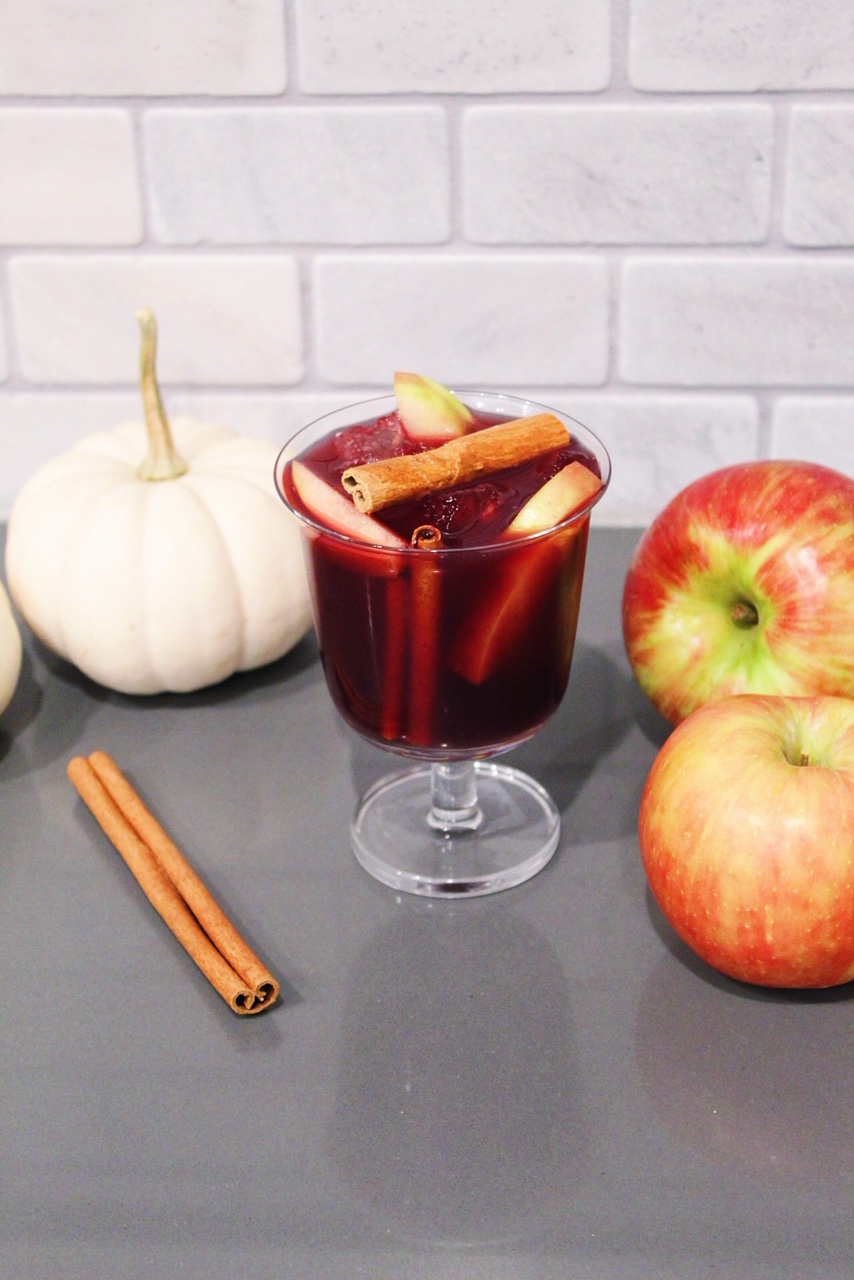 Red wine apple cider sangria in a glass with pumpkins and apples.