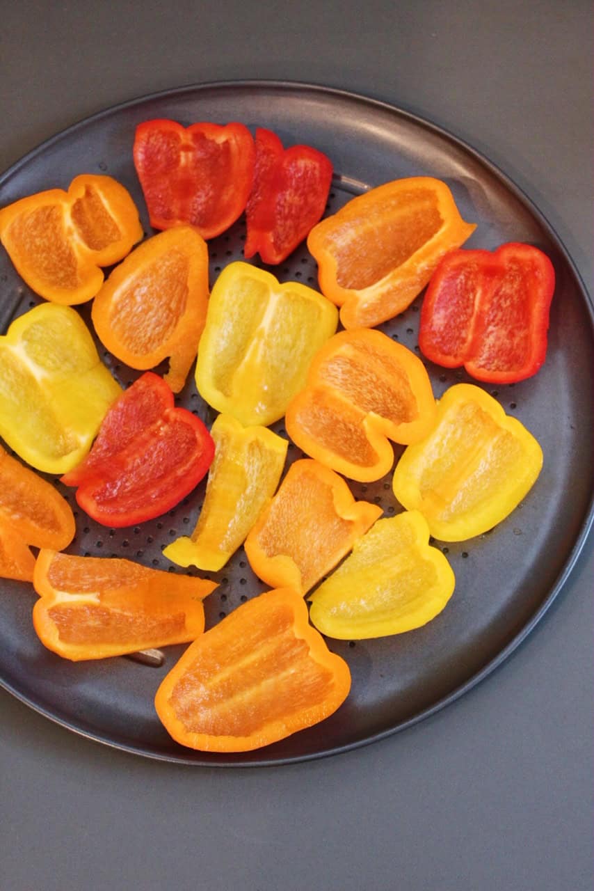 Red, orange, and yellow bell peppers halved on a sheet pan.