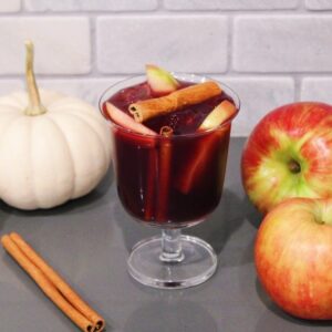 Thanksgiving Sangria in a glass with cinnamon sticks, apples, and pumpkins.