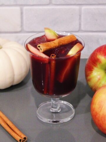 Thanksgiving Sangria in a glass with cinnamon sticks, apples, and pumpkins.