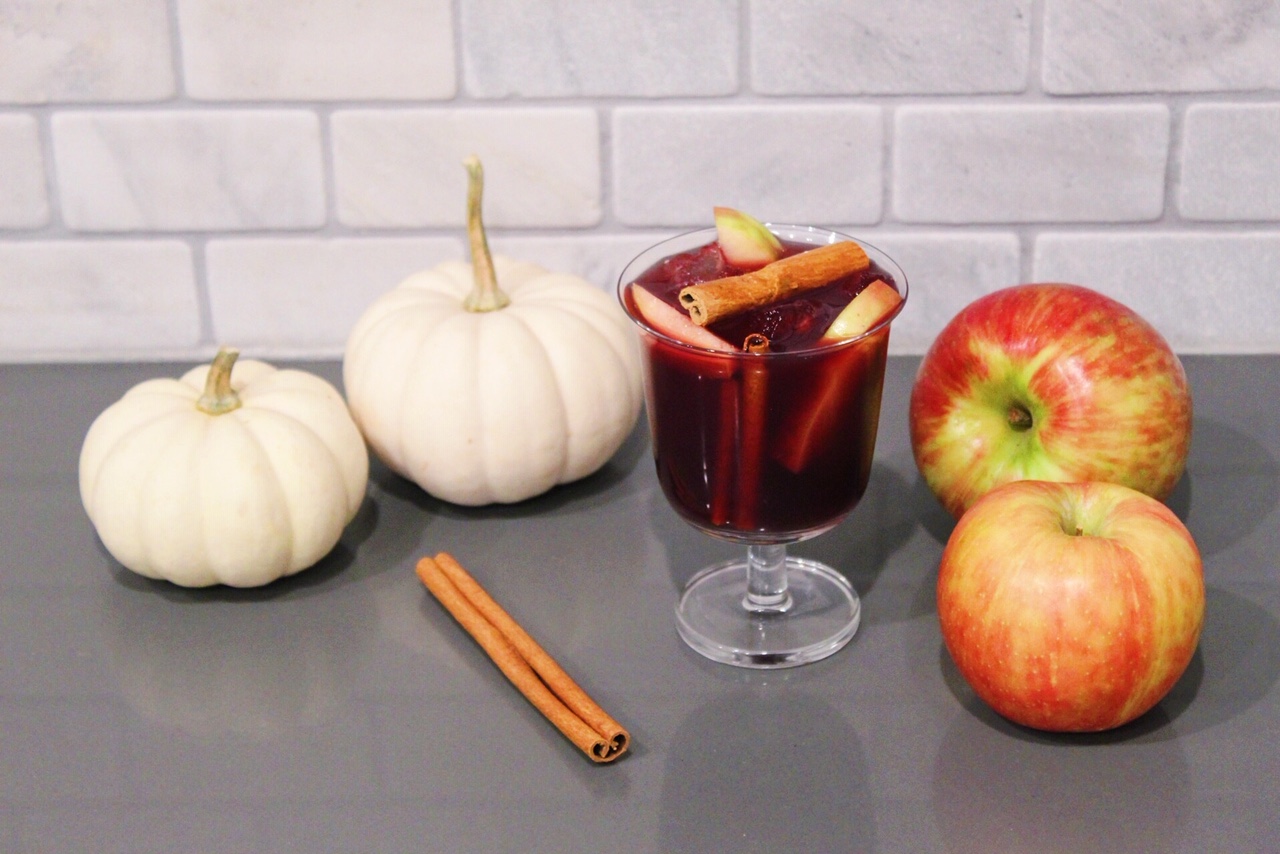 Thanksgiving Sangria topped with cinnamon sticks sitting next to pumpkins and apples.