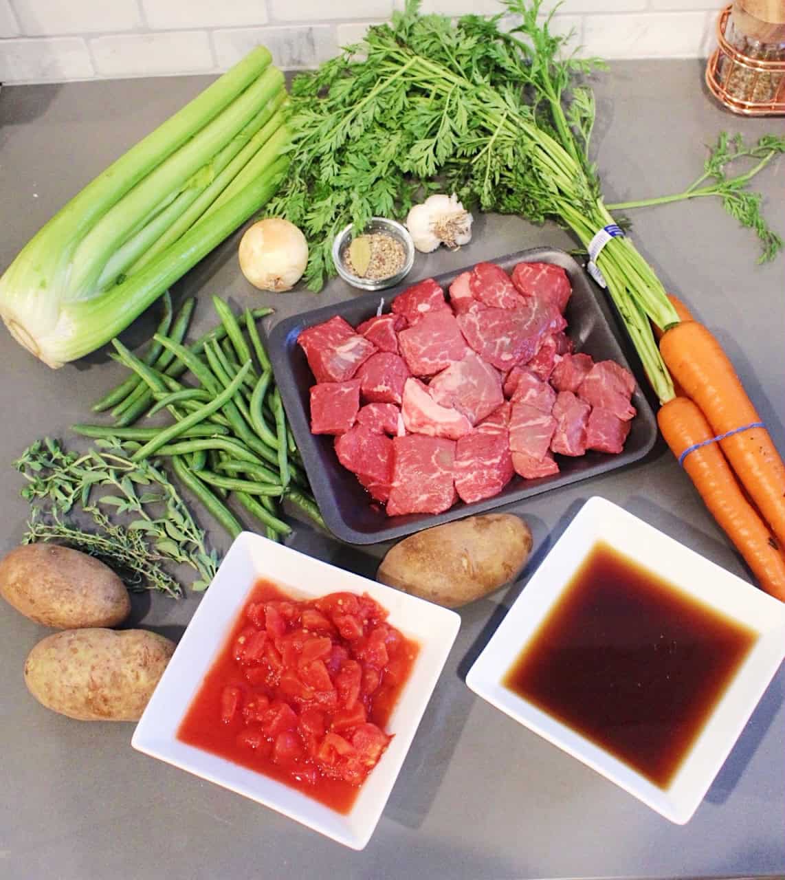 Ingredients for vegetable beef soup on a grey countertop.