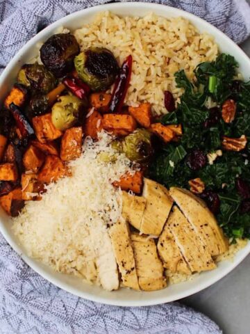 Fall harvest bowls containing rice, roasted vegetables, kale, and cheese in a white bowl.