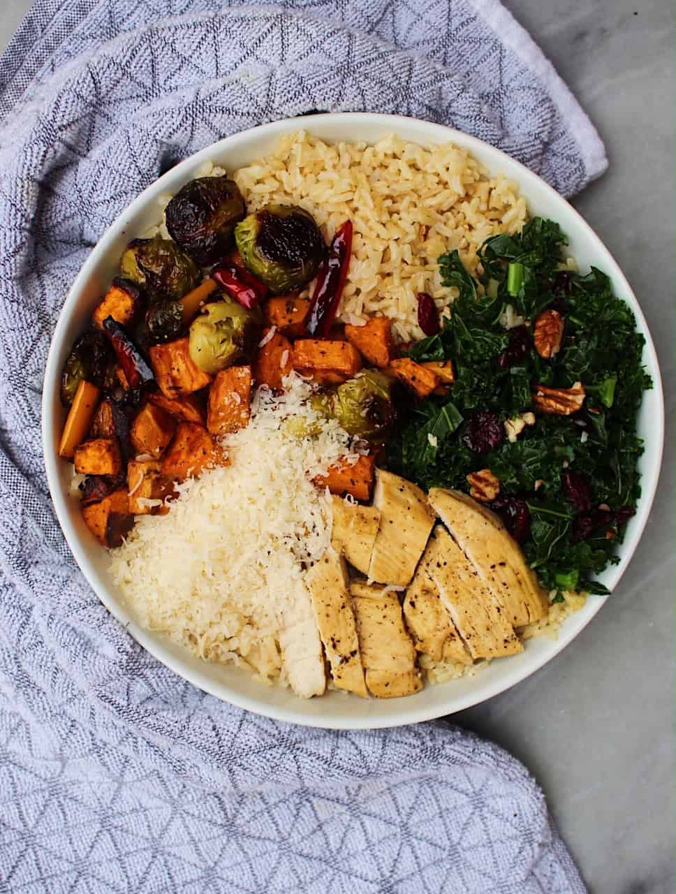 Fall harvest bowls containing rice, roasted vegetables, kale, and cheese in a white bowl.