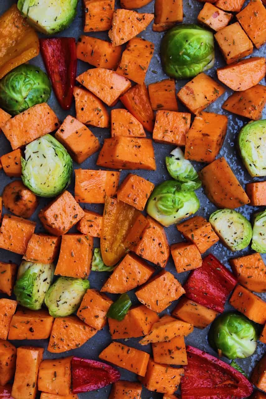 Sweet potatoes, Brussels sprouts, and peppers on a baking sheet.