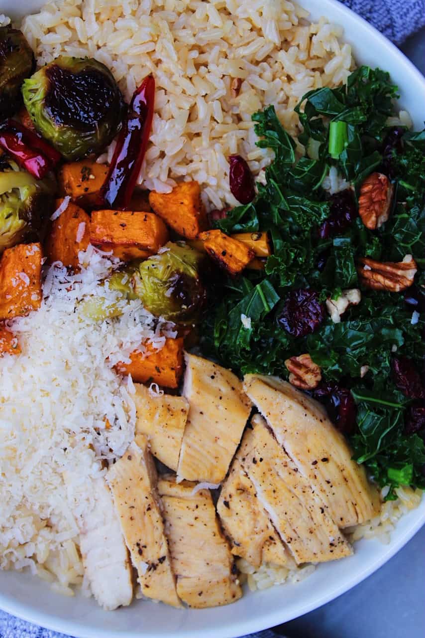 Close up of a bowl with chicken, kale, rice, brussels sprouts, and Parmesan.