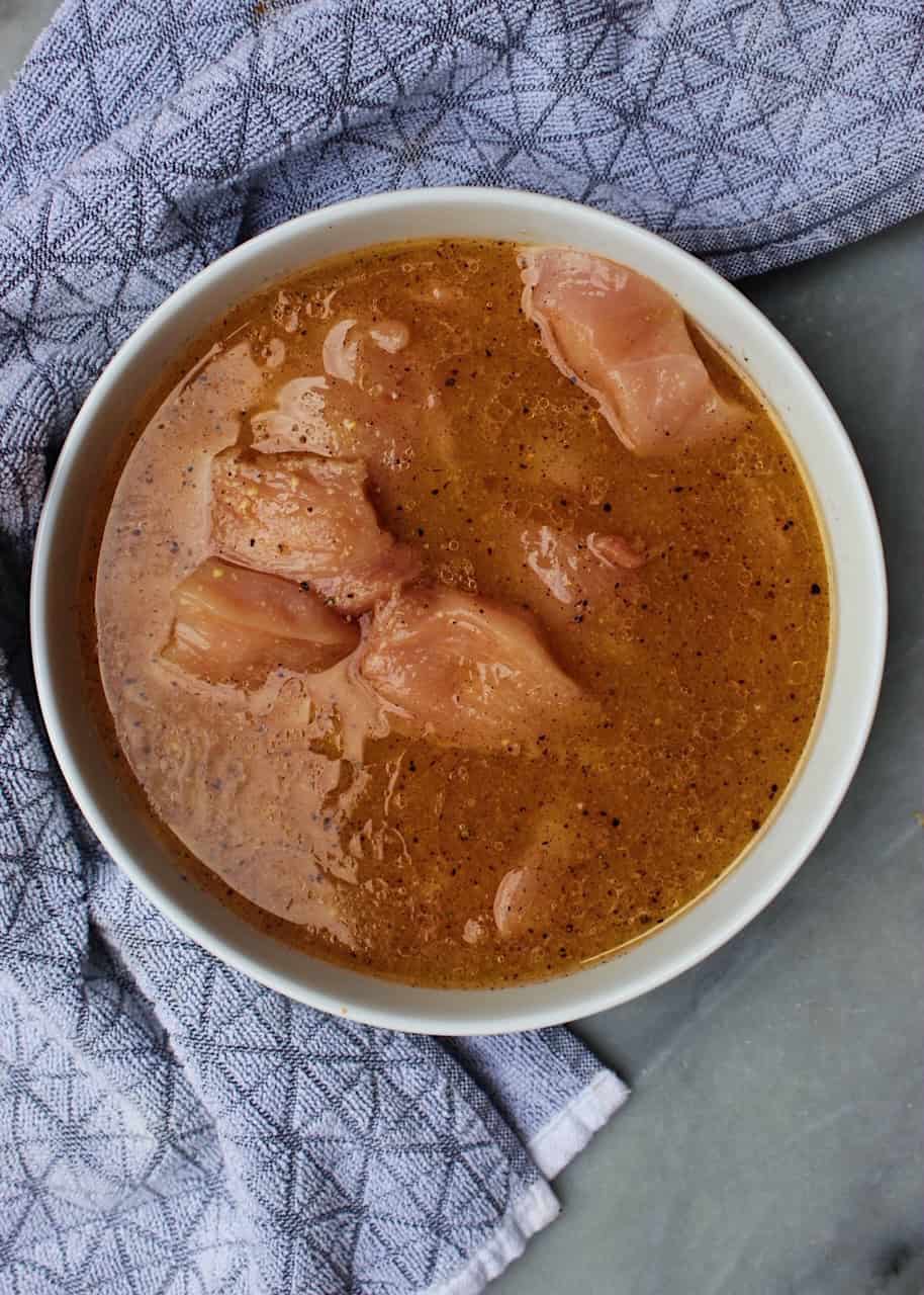 Chicken marinating in apple cider marinade in white bowl.