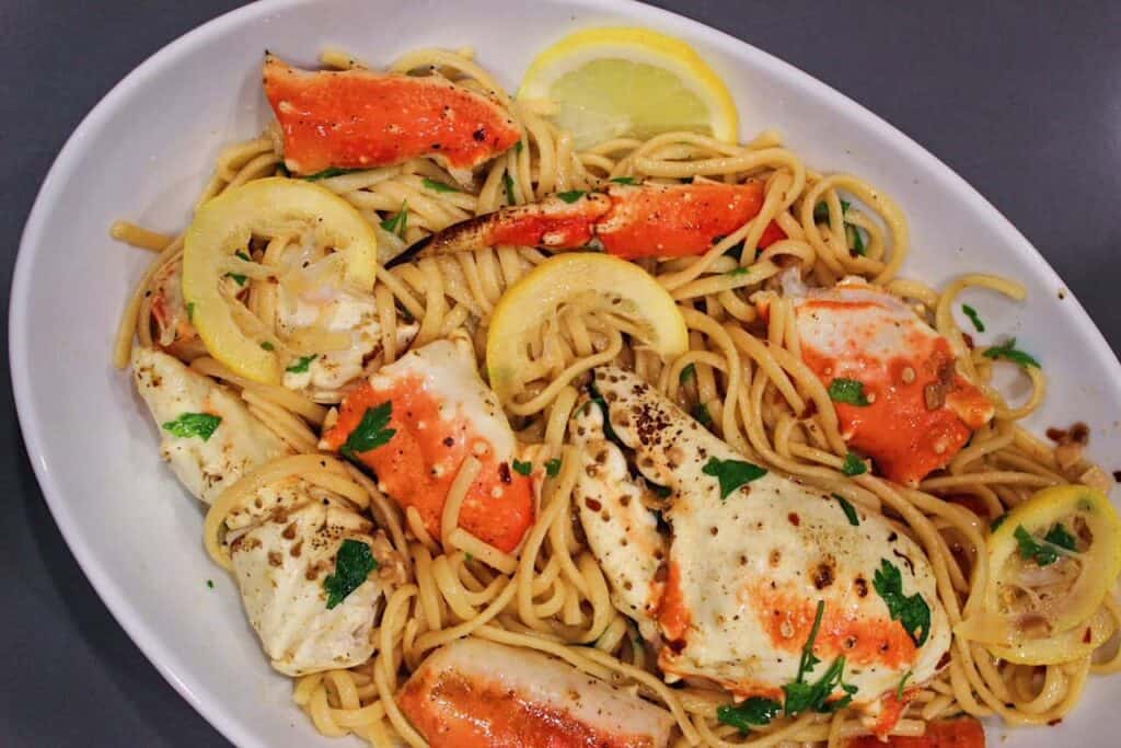 Crab Pasta in White Wine sauce tossed with lemon slices in large white serving bowl.