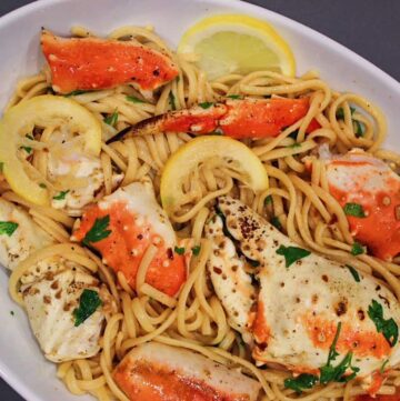 Crab Pasta in White Wine sauce tossed with lemon slices in large white serving bowl.