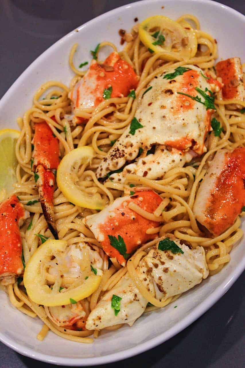 Crab legs and claws tossed with linguine and lemon slices in serving bowl.