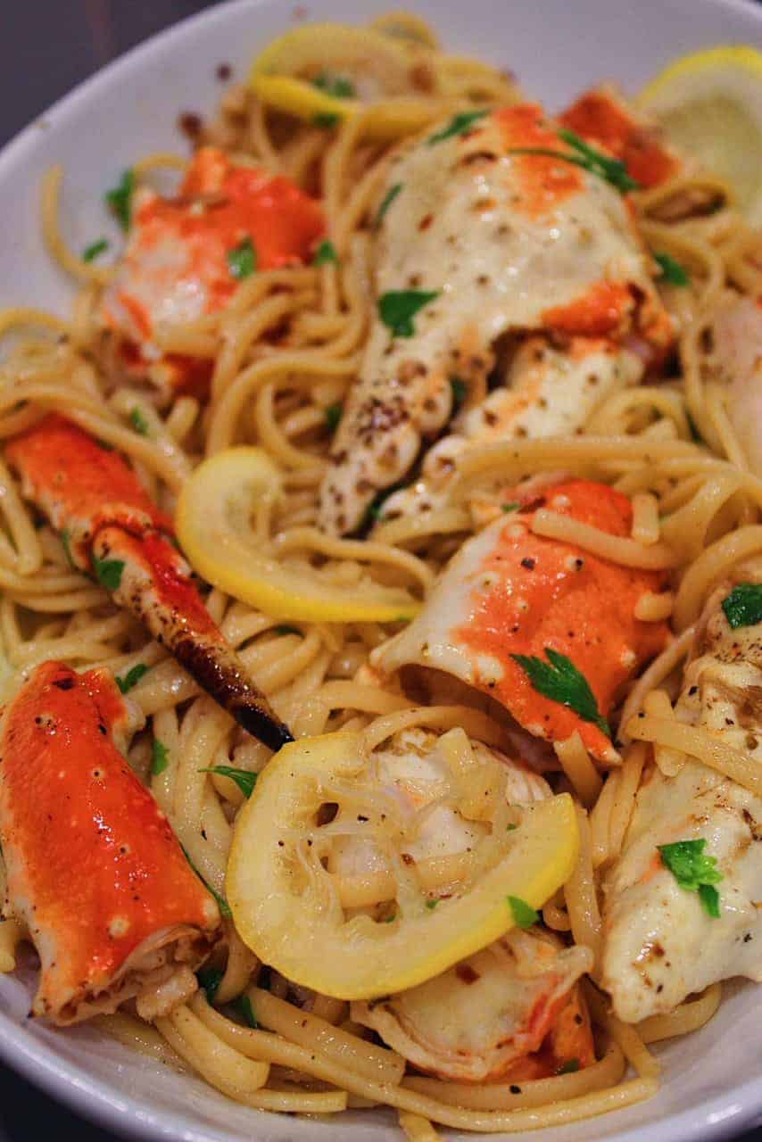 Crab legs and claws mixed with pasta in serving dish.