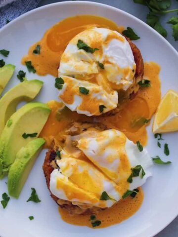 Overhead shot of Crab Cakes Eggs Benedict on a white plate with avocado.