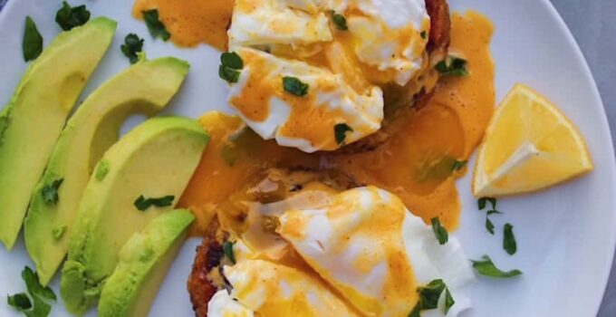 Overhead shot of Crab Cakes Eggs Benedict on a white plate with avocado.