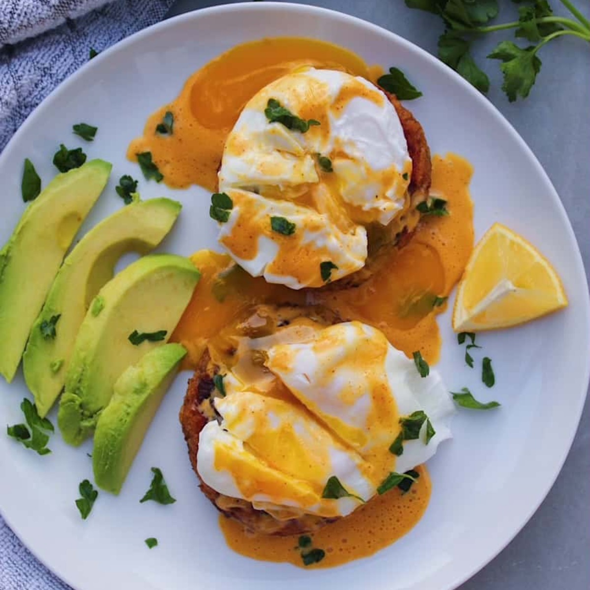 Overhead shot of Crab Cakes Eggs Benedict on a white plate with avocado.