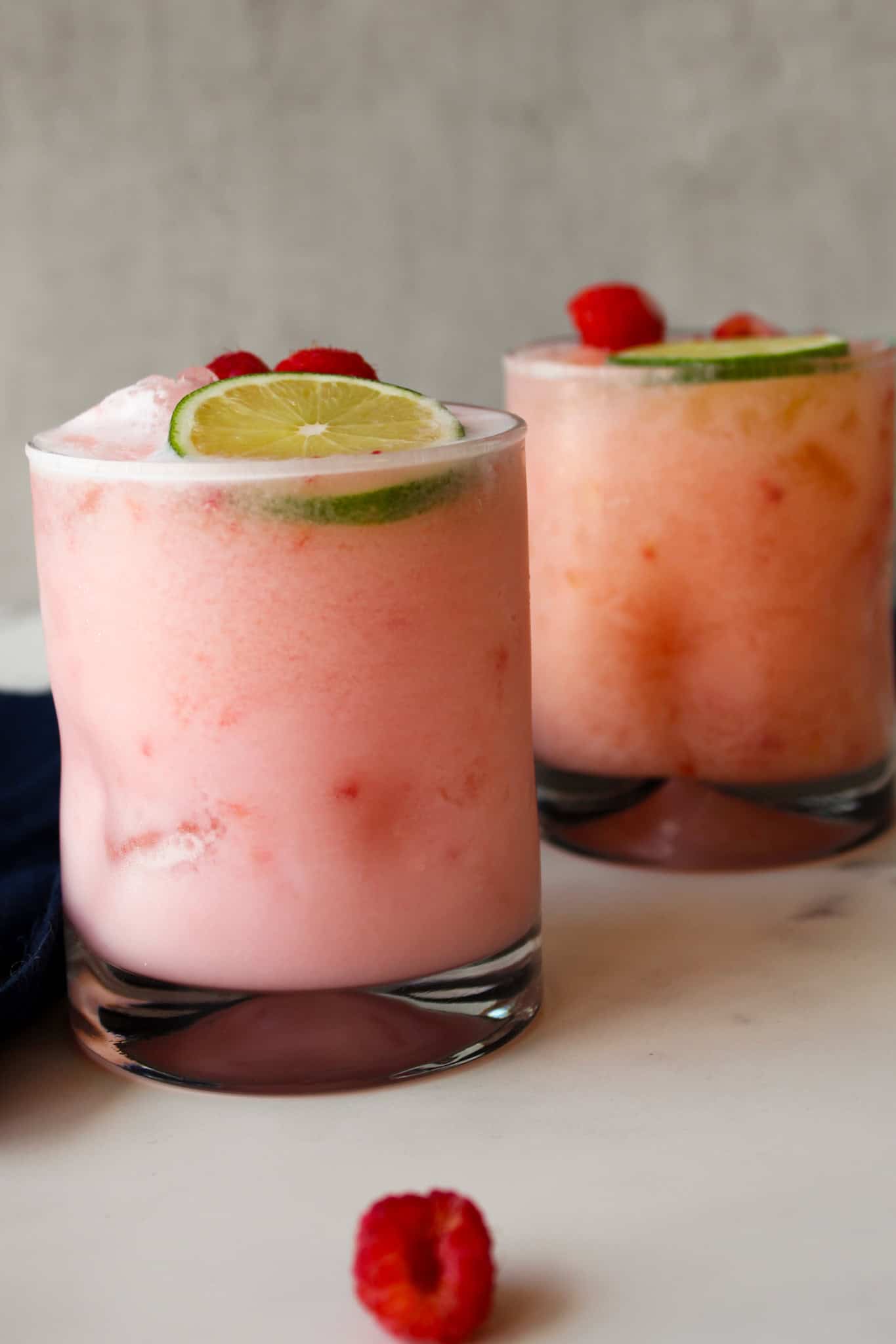 Side view of two pale pink coconut margaritas with fresh raspberries.