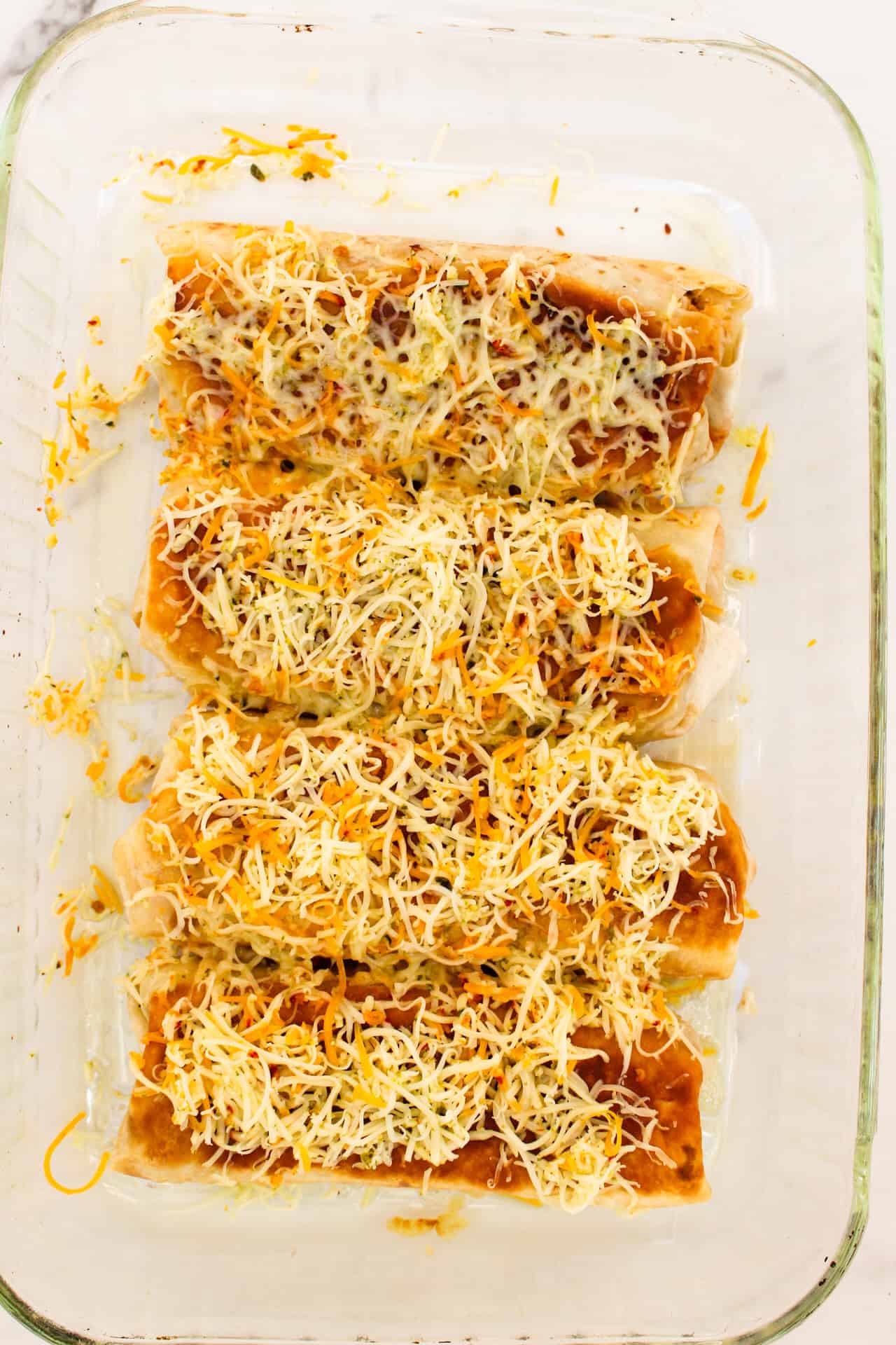 Adding cheese to tops of burritos in baking dish.