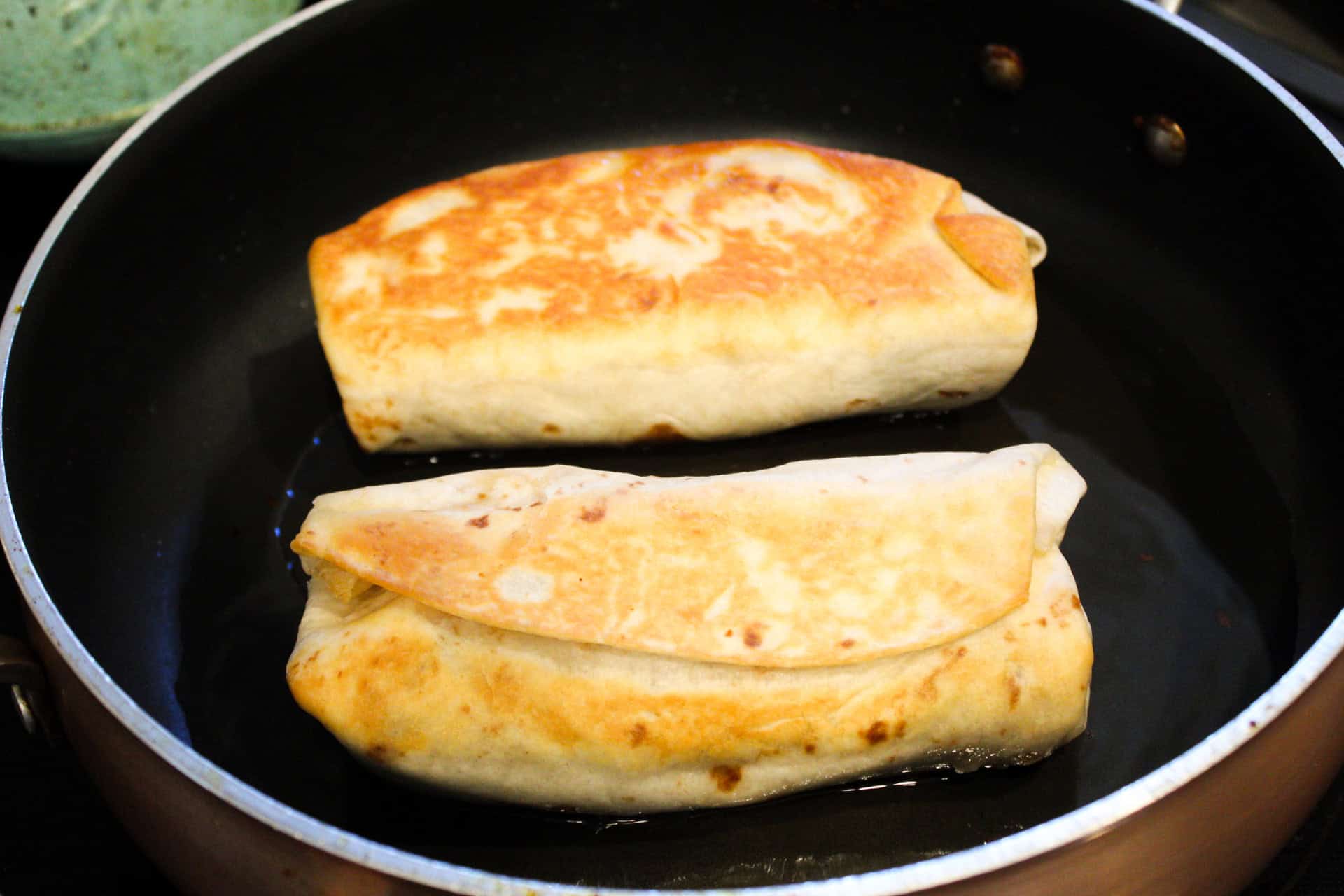 Burritos in a skillet being pan fried. 