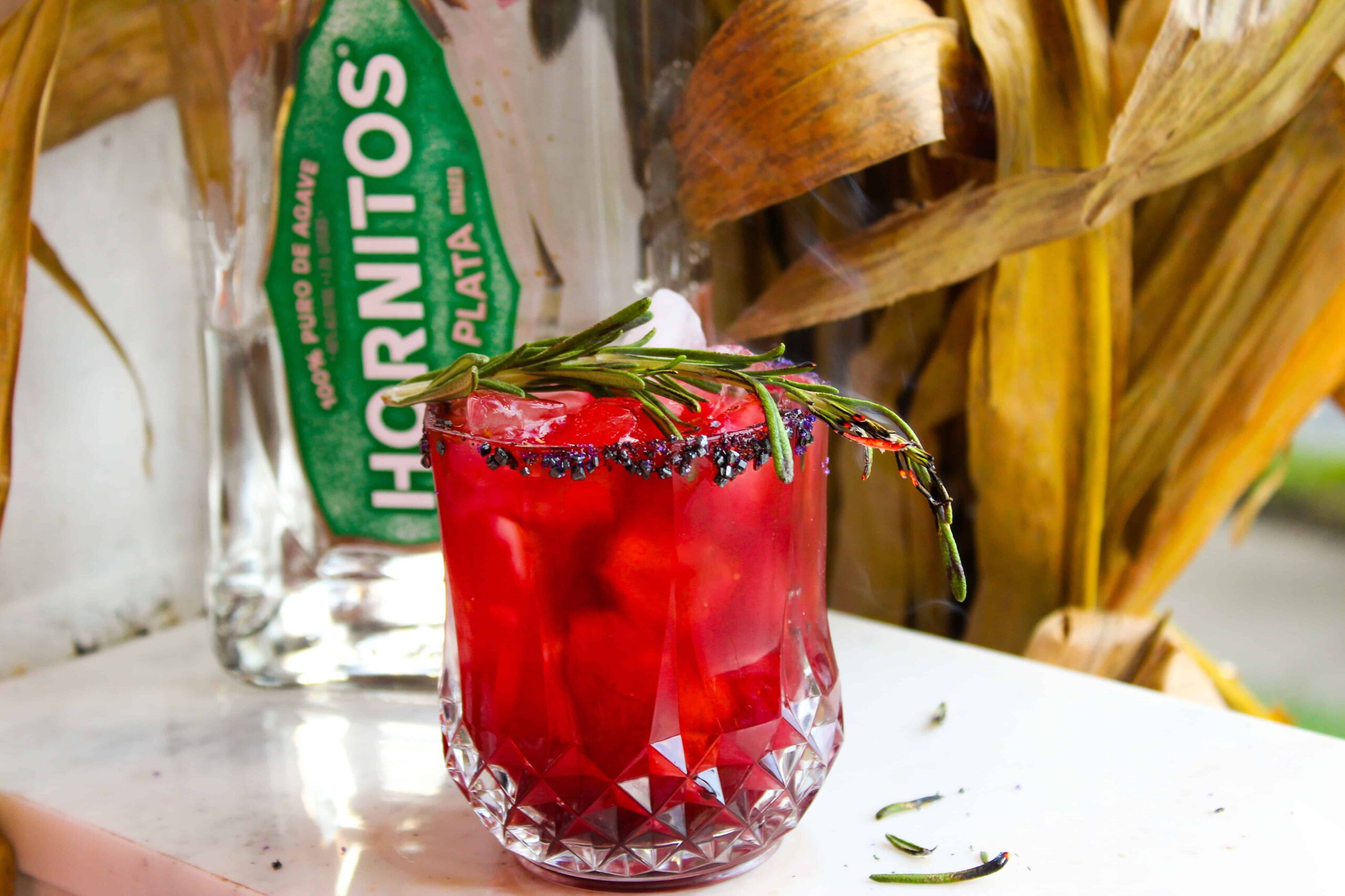 Red margarita in a rocks glass next to a bottle of Hornitos tequila.