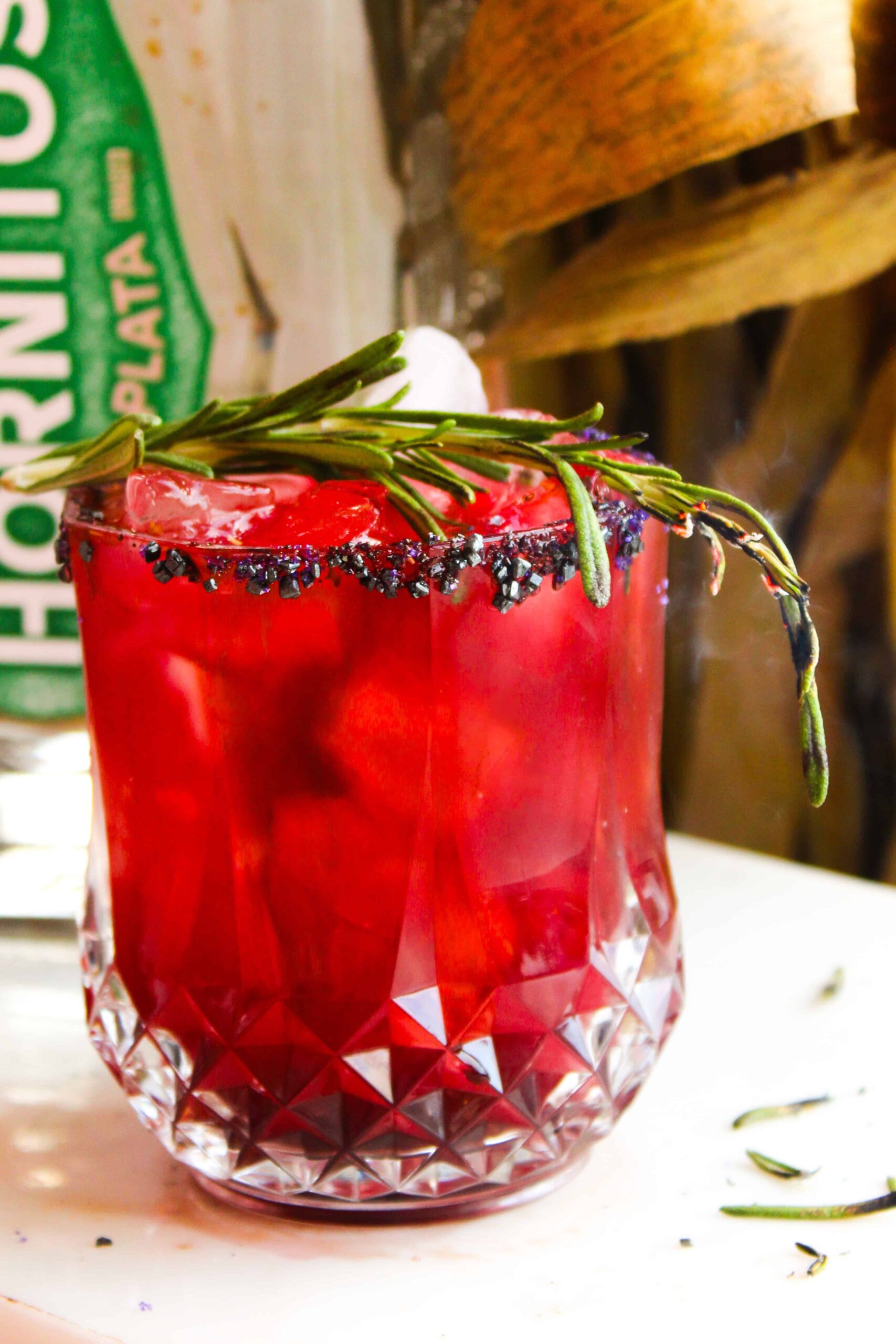 Close up of bright red margarita with black sugar rim and smoking rosemary garnish.